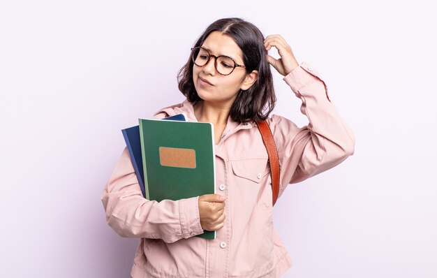 Bela jovem se sentindo perplexa e confusa, coçando a cabeça. estudante com conceito de livros