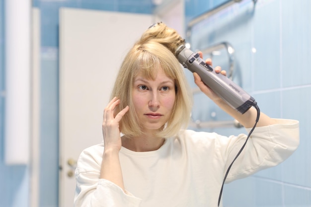 Bela jovem seca e estiliza seu secador de cabelo