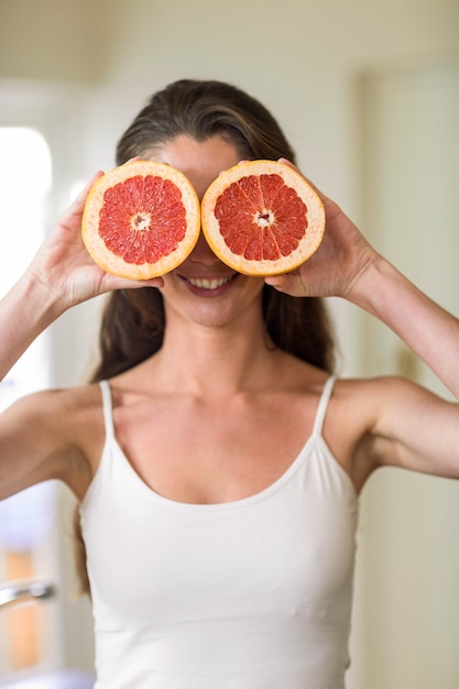 Bela jovem segurando fatias de laranja de sangue na cozinha