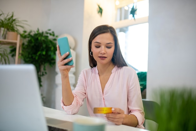 Bela jovem segurando seu smartphone enquanto paga com cartão de crédito