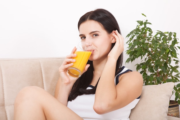 Bela jovem segurando um copo com suco de laranja na mão e bebida em casa