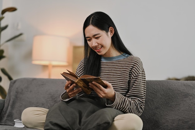 Bela jovem sentada em um sofá aconchegante e lendo um livro Pessoas conceito de lazer e estilo de vida