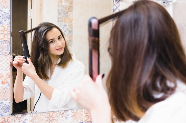 Bela jovem sexy faz um alisador de cabelo pelo espelho Beleza e cuidados com o cabelo