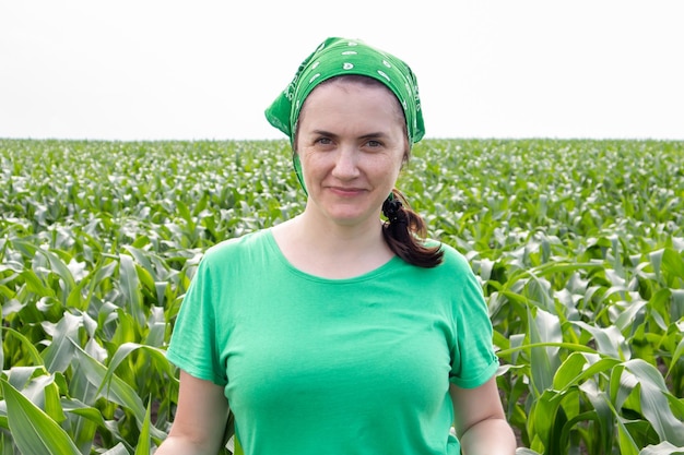Foto bela jovem sorridente agricultor em t-shirt verde e chapéu de sol verde em pé no meio de um campo de milho verde em um dia ensolarado de verão ao ar livre. tempo de colheita. agricultura orgânica. luz solar.
