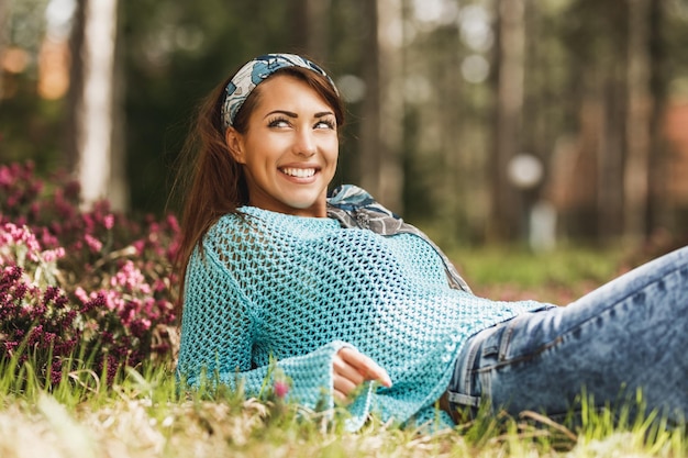 Bela jovem sorridente deitada na grama florida e aproveitando o dia ensolarado de primavera.