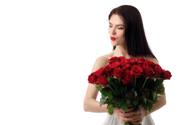 Bela jovem sorridente em um vestido branco com um grande buquê de rosas vermelhas em um fundo branco