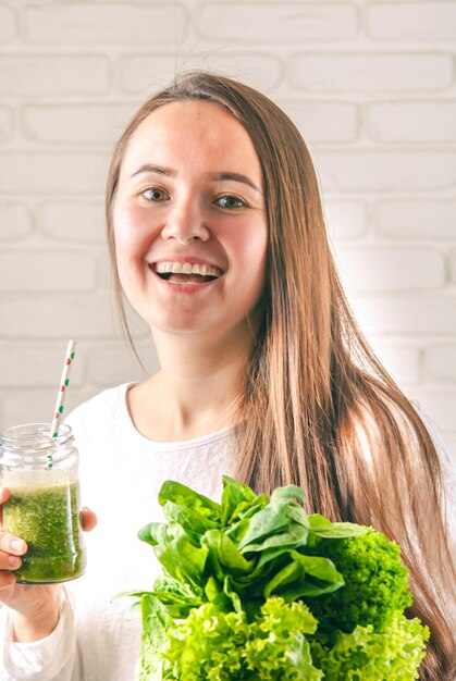 bela jovem sorridente está bebendo shake de desintoxicação verde