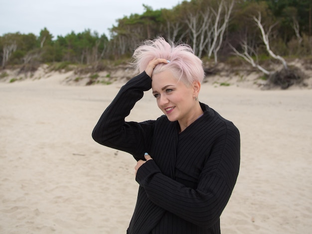 Foto bela jovem sorridente feliz modelo com cabelo rosa e corte de cabelo na moda posando na praia