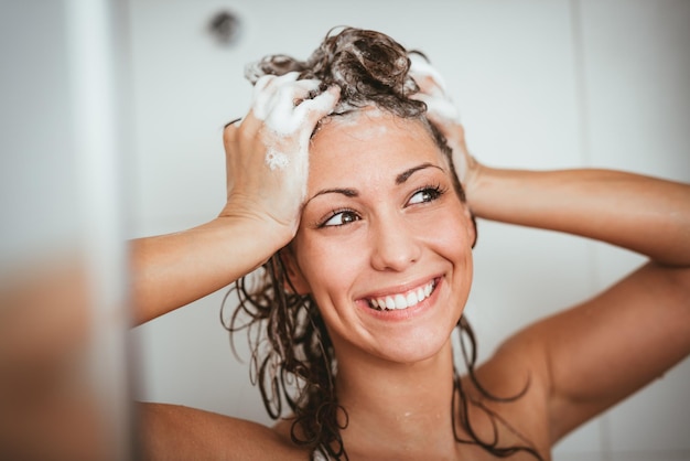 Foto bela jovem sorridente lavando o cabelo comprido com shampoo.