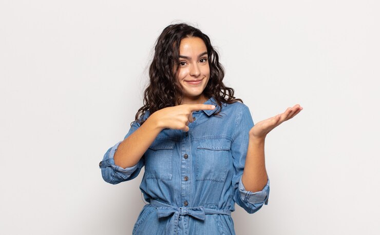 Foto bela jovem sorrindo alegremente e apontando para copiar o espaço na palma da mão ao lado, mostrando ou anunciando um objeto