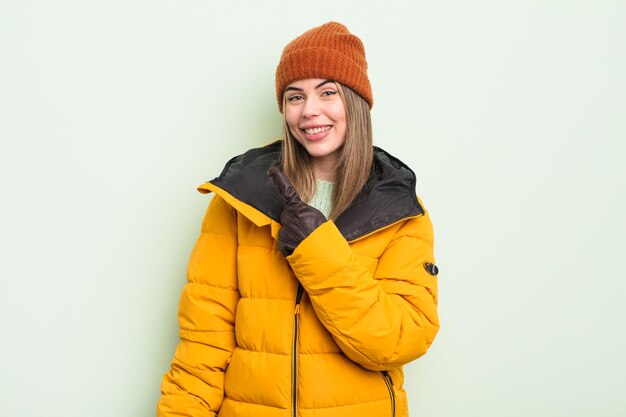 Bela jovem sorrindo alegremente sentindo-se feliz e apontando para o conceito de clima frio lateral