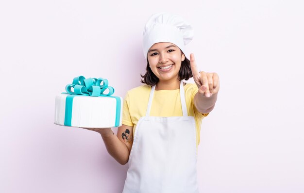 Bela jovem sorrindo e parecendo amigável, mostrando o número um. chef cozinhando um bolo