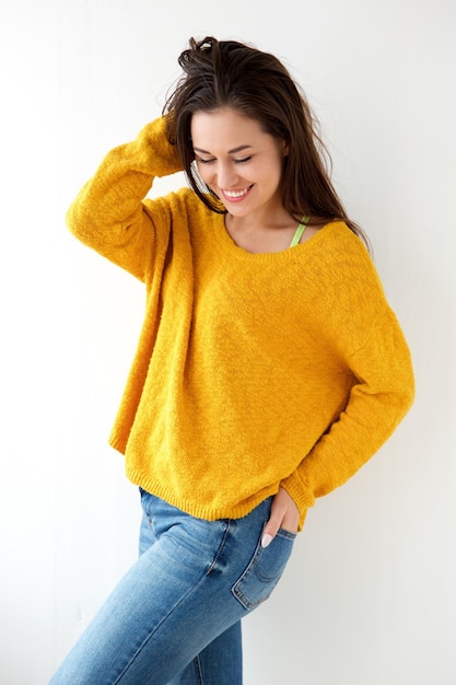 Foto bela jovem sorrindo em suéter amarelo contra a parede branca