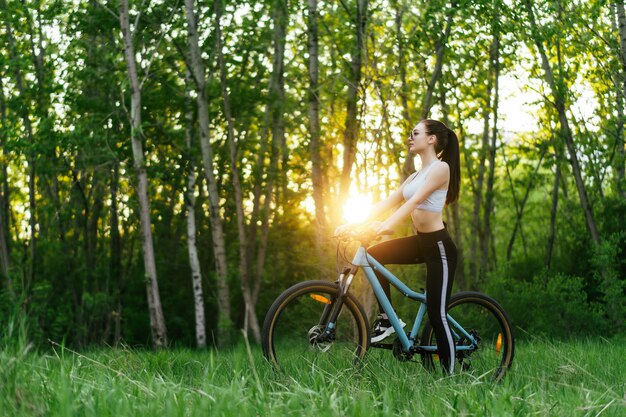 Bela jovem tem um passeio de bicicleta em um parque no pôr do sol