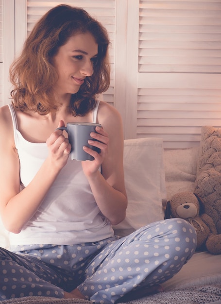 Bela jovem tomando café sentado na cama em casa