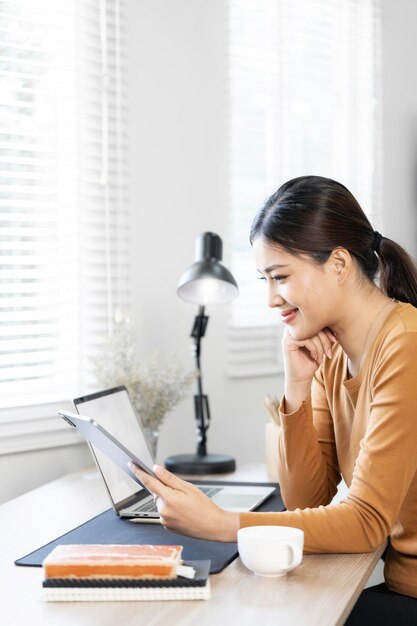 Bela jovem trabalhando em tablet e computador portátil enquanto sentada na sala de estar