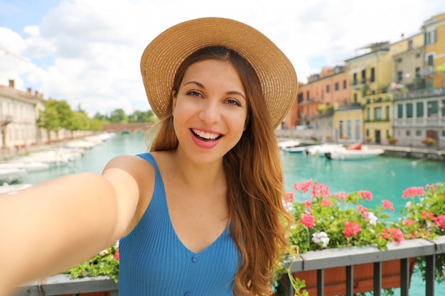 Bela jovem turista tira auto-retrato no Lago de Garda, Itália. Menina bonita da moda tira foto de selfie em Peschiera del Garda, Itália.