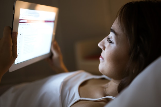 Foto bela jovem usando seu tablet digital na cama à noite.