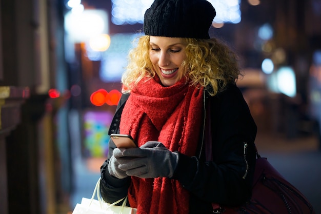 Bela jovem usando seu telefone celular na rua à noite.