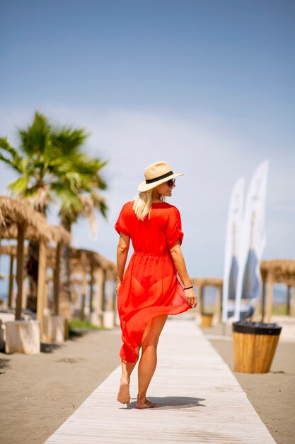 Bela jovem vestida de vermelho caminhando em uma praia no verão