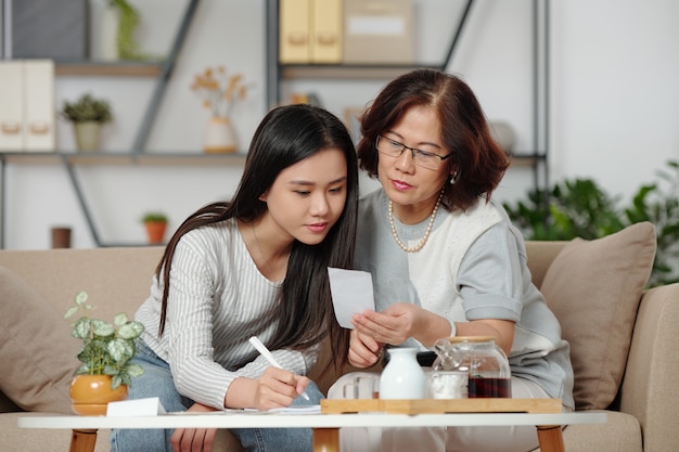 Bela jovem vietnamita checando contas e ajudando a mãe com a contabilidade doméstica