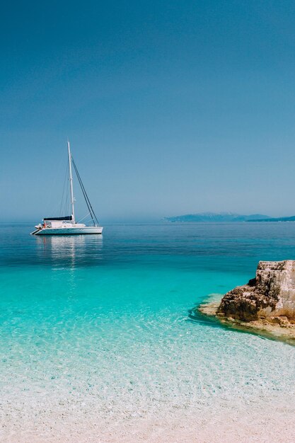 Bela lagoa azul-azulada com catamarã a vela, iate ancorado, praia de seixos brancos puros.