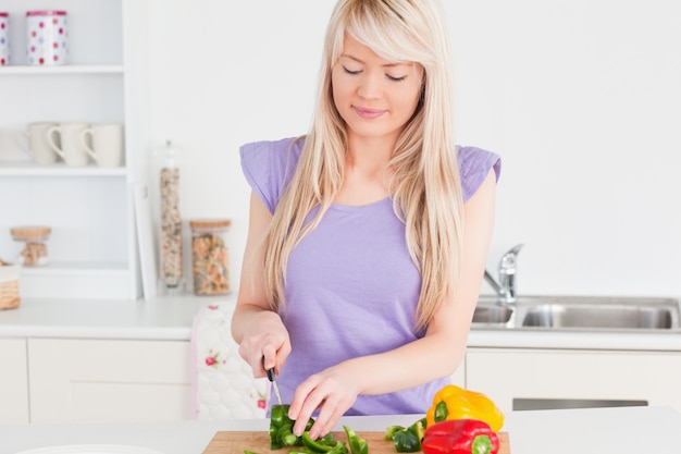 Bela loira feminina cortando vegetais no interior da cozinha moderna