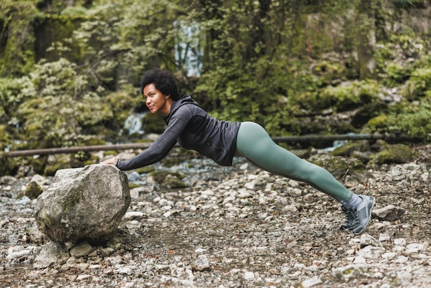 Bela madura corredora afro-americana fazendo treinamento de aquecimento na natureza.