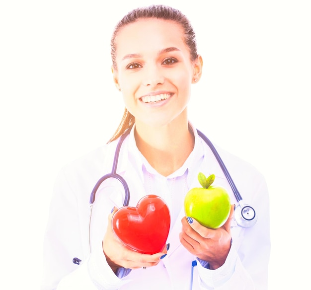 Bela médica sorridente segurando um coração vermelho e uma maçã verde.