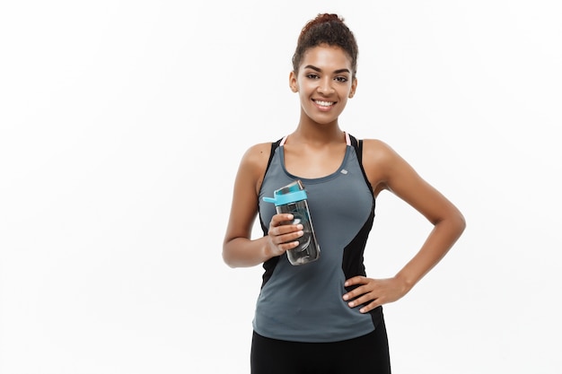 Foto bela menina afro-americana em roupas esportivas segurando garrafa de água após o treino.