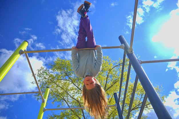 Foto bela menina loira com cabelos longos brincando no playground menina pendurada de cabeça para baixo em um parque
