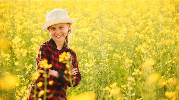 Bela menina sorridente com chapéu de pé flor amarela colza cruzou os braços e