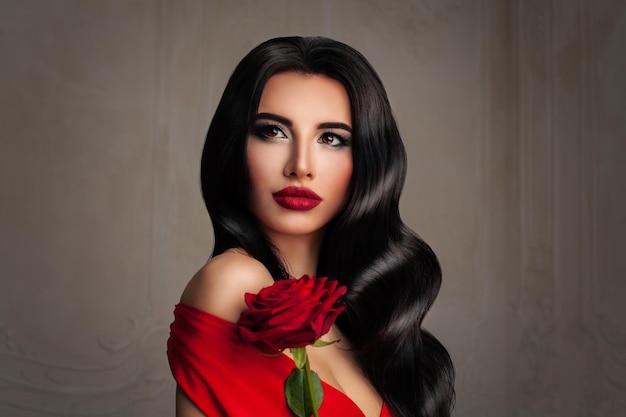 Bela moça. Retrato da moda da mulher perfeita com maquiagem morena cabelo e evento. Penteado encaracolado, lábios vermelhos e flor de rosa vermelha