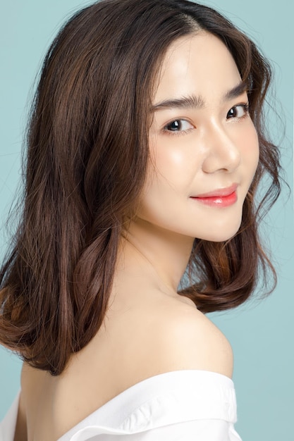 Bela modelo asiática de cabelo curto com maquiagem natural e pele limpa e fresca em fundo azul