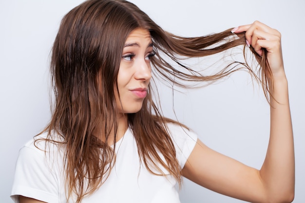 Bela modelo feminino jovem cuida do cabelo dela e usa um alisador de cabelo