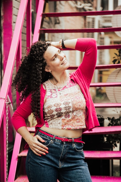 Foto bela modelo sorridente com penteado de cachos afro e vestido com roupas rosa hippie.