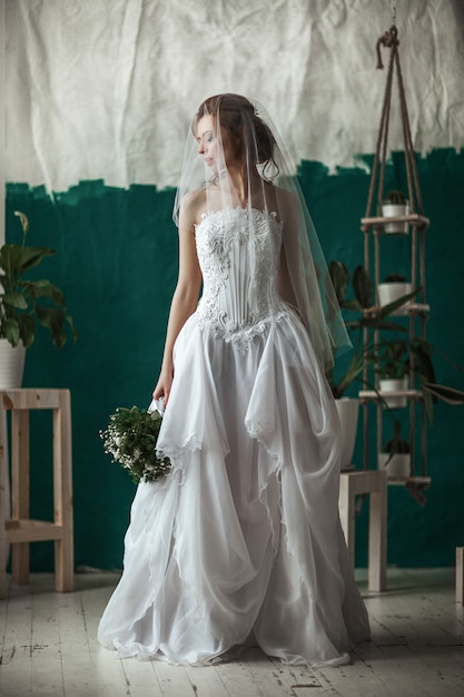 Bela modelo usando vestido de renda branca está posando em um estúdio de interior