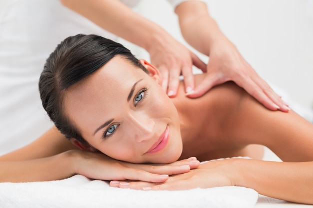 Bela morena, desfrutando de uma massagem nos ombros, sorrindo para a câmera no spa de saúde