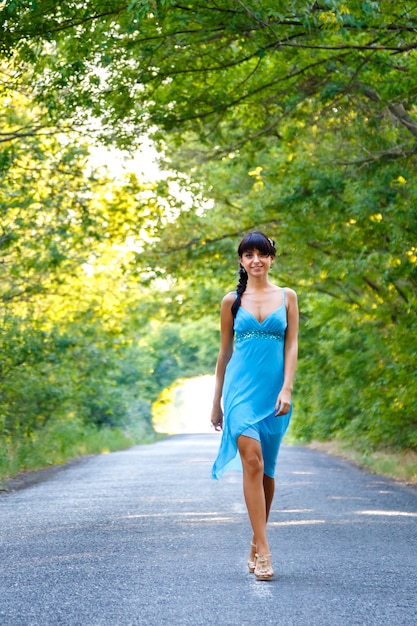 Bela morena jovem caminhando na estrada vazia no dia de verão