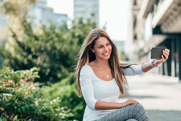 Foto bela morena jovem tomando um selfie na cidade.