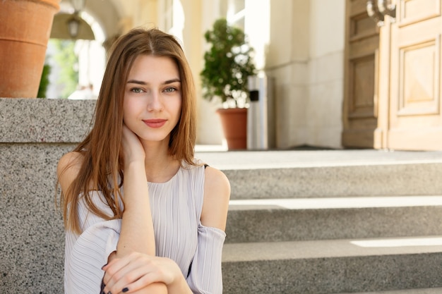 Bela morena jovem vestindo roupas da moda, sentada nas escadas em uma cidade velha.