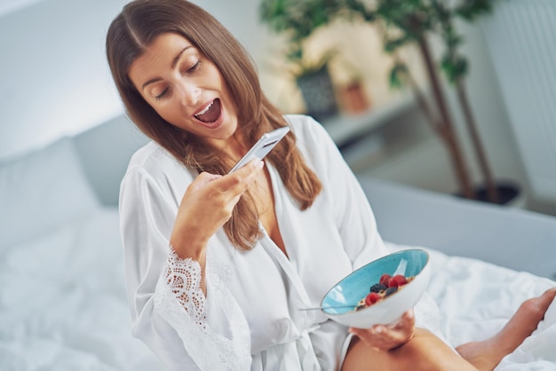 Bela morena na cama com café da manhã de cereais com telefone