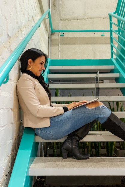 Bela morena trabalhando com seu laptop na escada