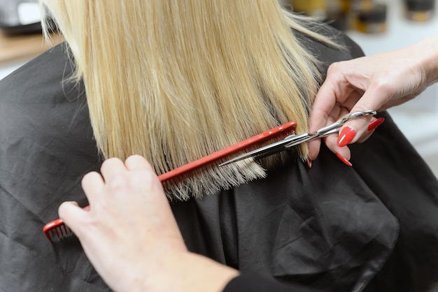 Bela morena trabalhando como cabeleireira corta as pontas do cabelo do cliente em um salão de beleza