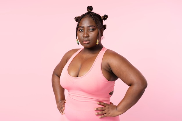 Bela mulher africana pensativa em roupas esportivas sutiã rosa treinamento isolado em fundo rosa corpo alegre modelo positivo de pé olhando para a câmera conceito de beleza cuidados de saúde