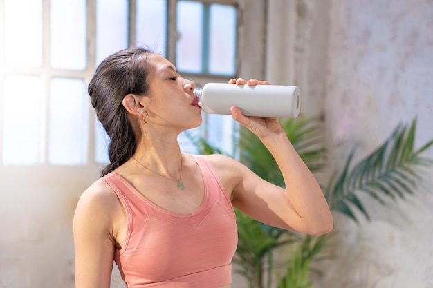 Bela mulher asiática esportiva a beber água de uma cantina conceito de estilo de vida saudável