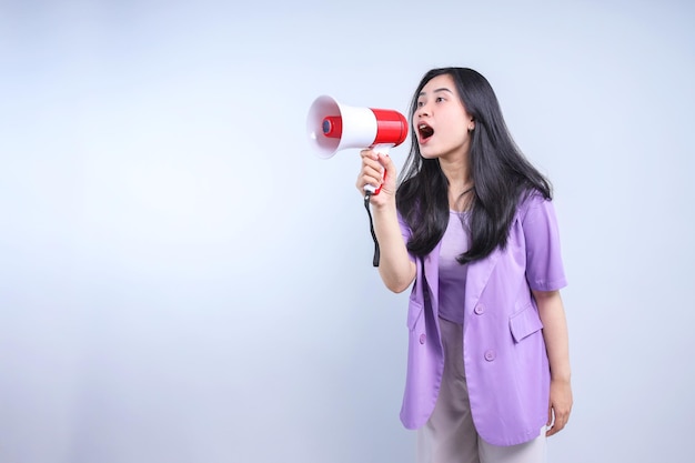 Bela mulher asiática excitada gritando e segurando megafone em fundo cinza