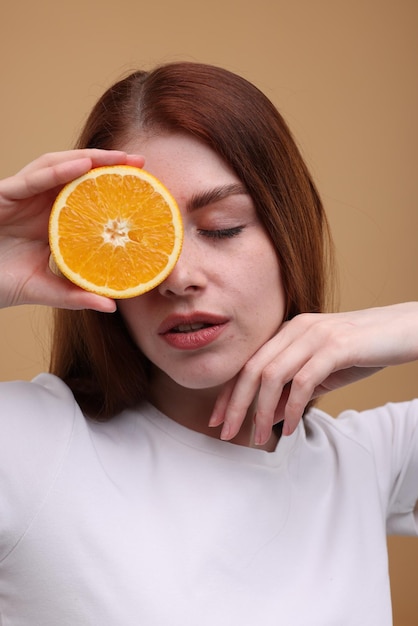 Bela mulher cobrindo o olho com metade de laranja em fundo bege