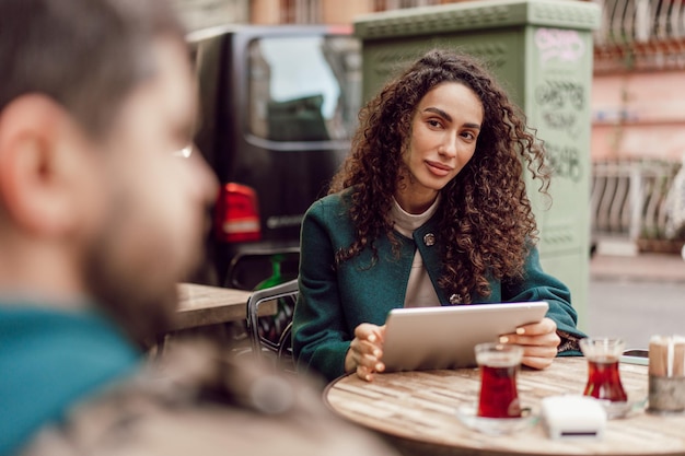 Foto bela mulher de negócios rizada usando tablet digital ao ar livre em um café