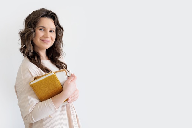 Bela mulher europeia de fato bege segura uma pilha de diários dourados e brancos com fundo branco